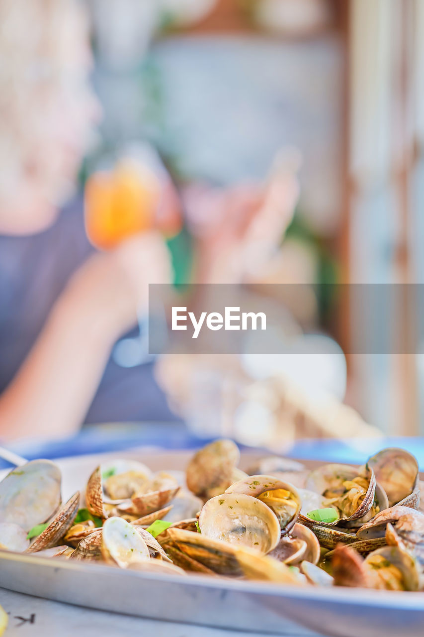 Blurred background, dish of boiled vongole clams,  silhouette of woman with  glass of wine