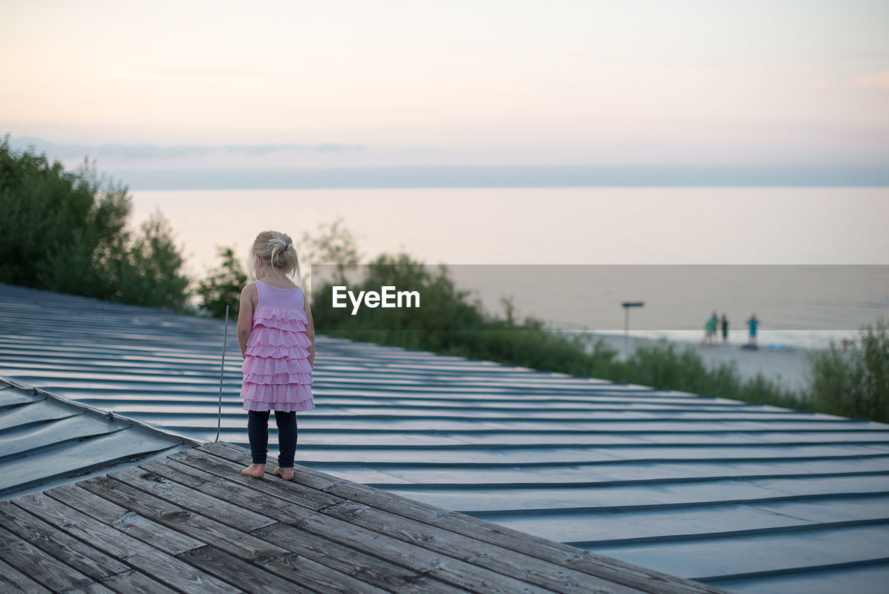 Rear view full length of girl standing on roof against sea