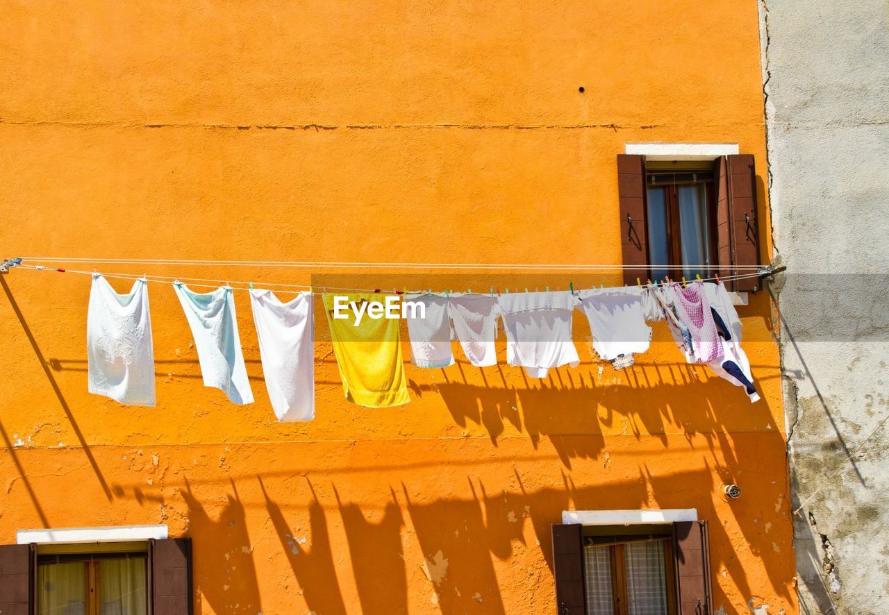 Clothes drying on rope against orange building during sunny day