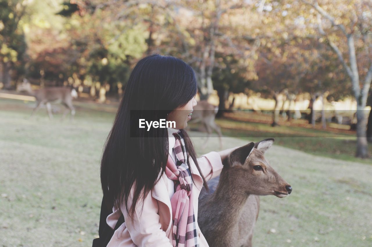 Side view of young woman with deer on field