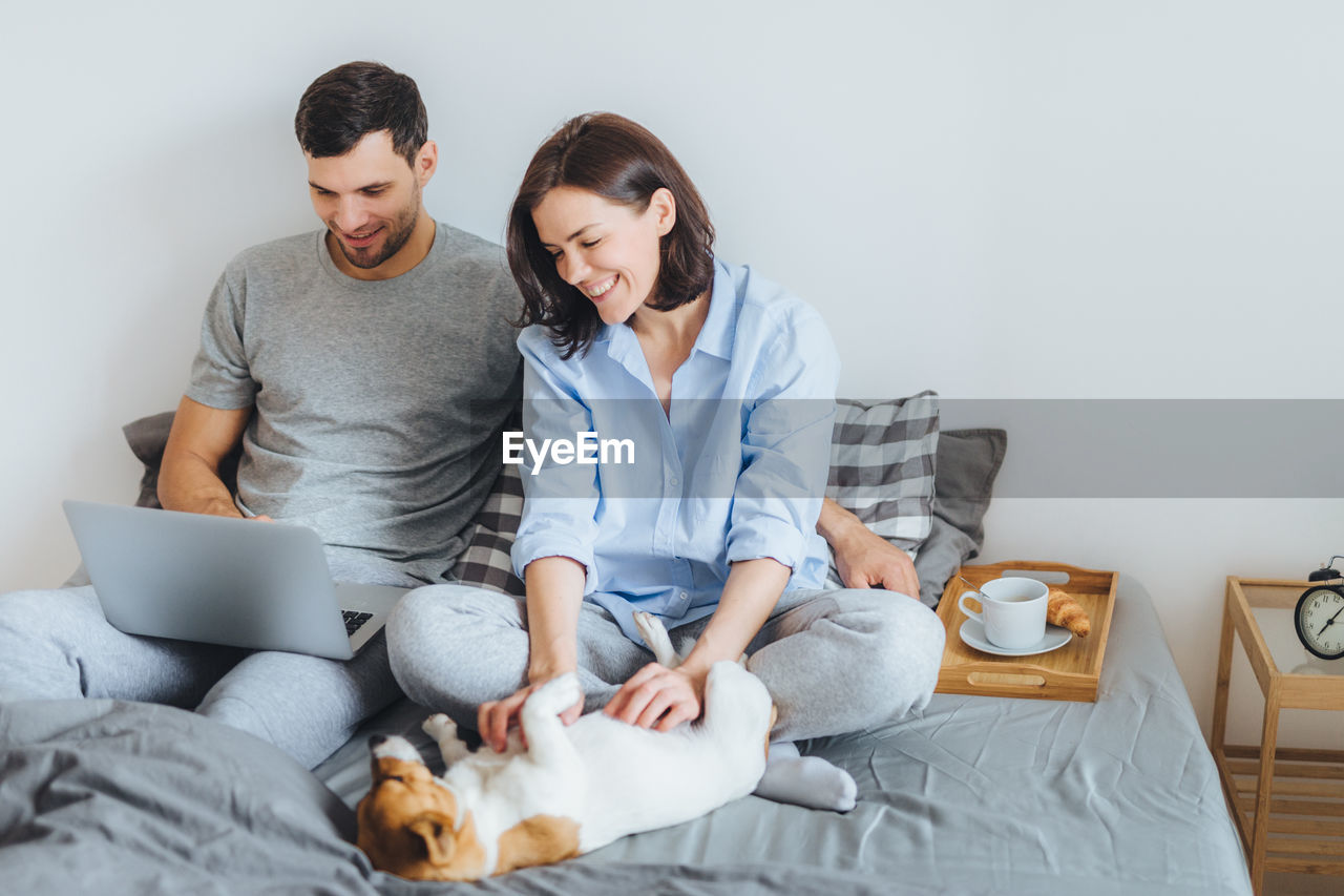 Couple with dog on bed against wall at home