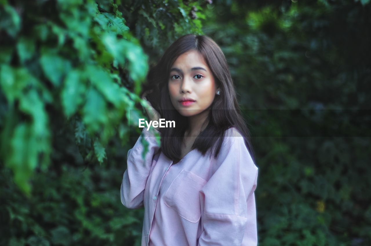 Portrait of young woman standing against trees in park