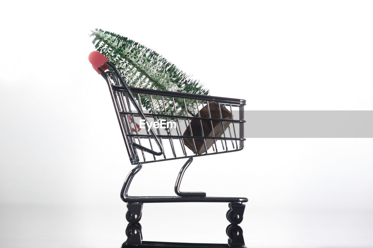 Close-up of christmas tree in miniature shopping cart against white background