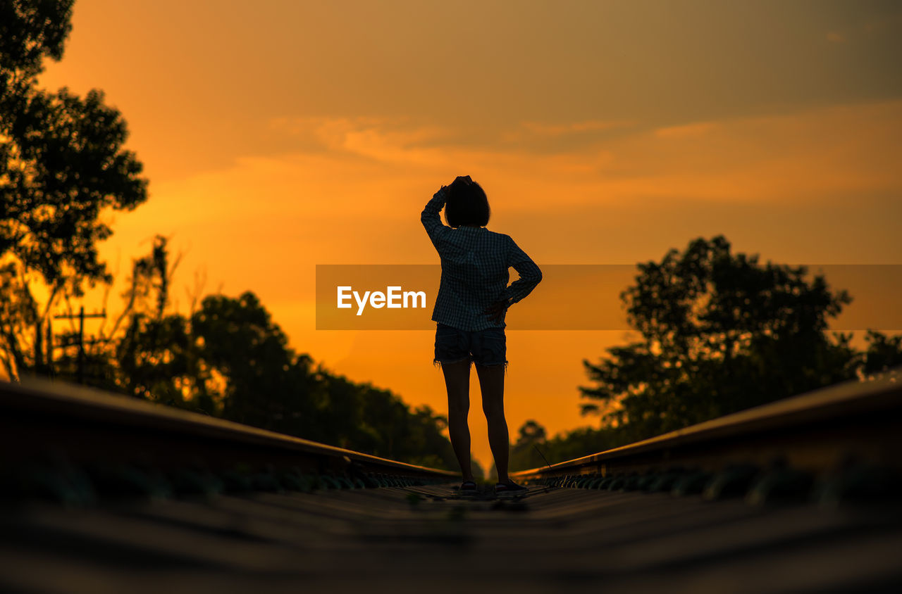 Full length of silhouette woman standing on railroad track while standing against sky during sunset