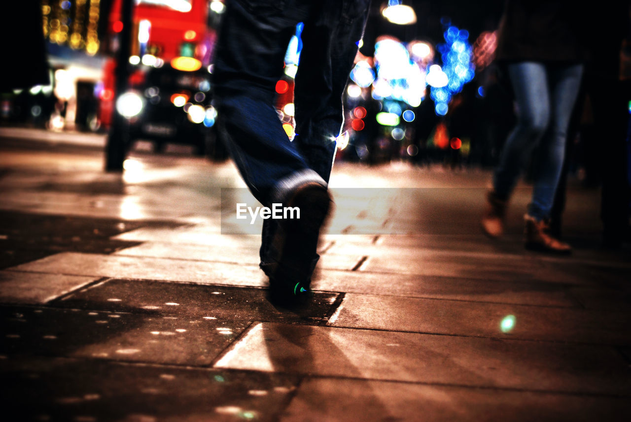 Low section of people walking on sidewalk in city at night