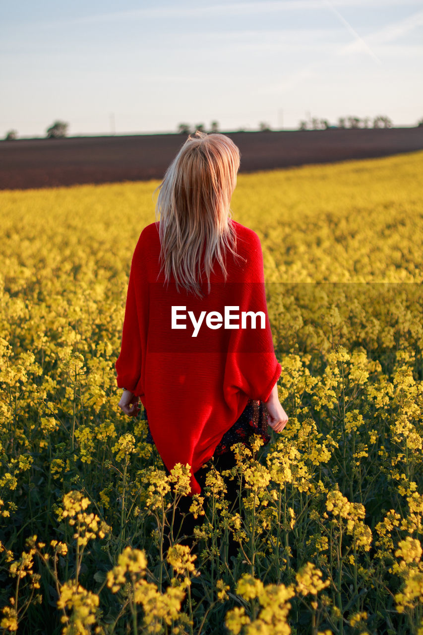 Rear view of woman standing amidst oilseed rape field against sky