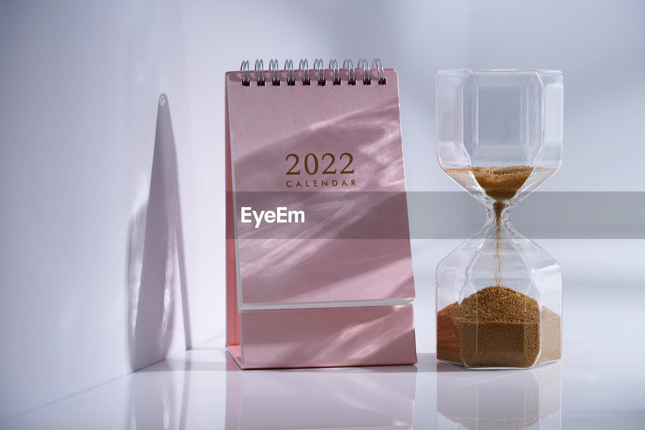 Hourglass with calendar on white desk close up. time concept