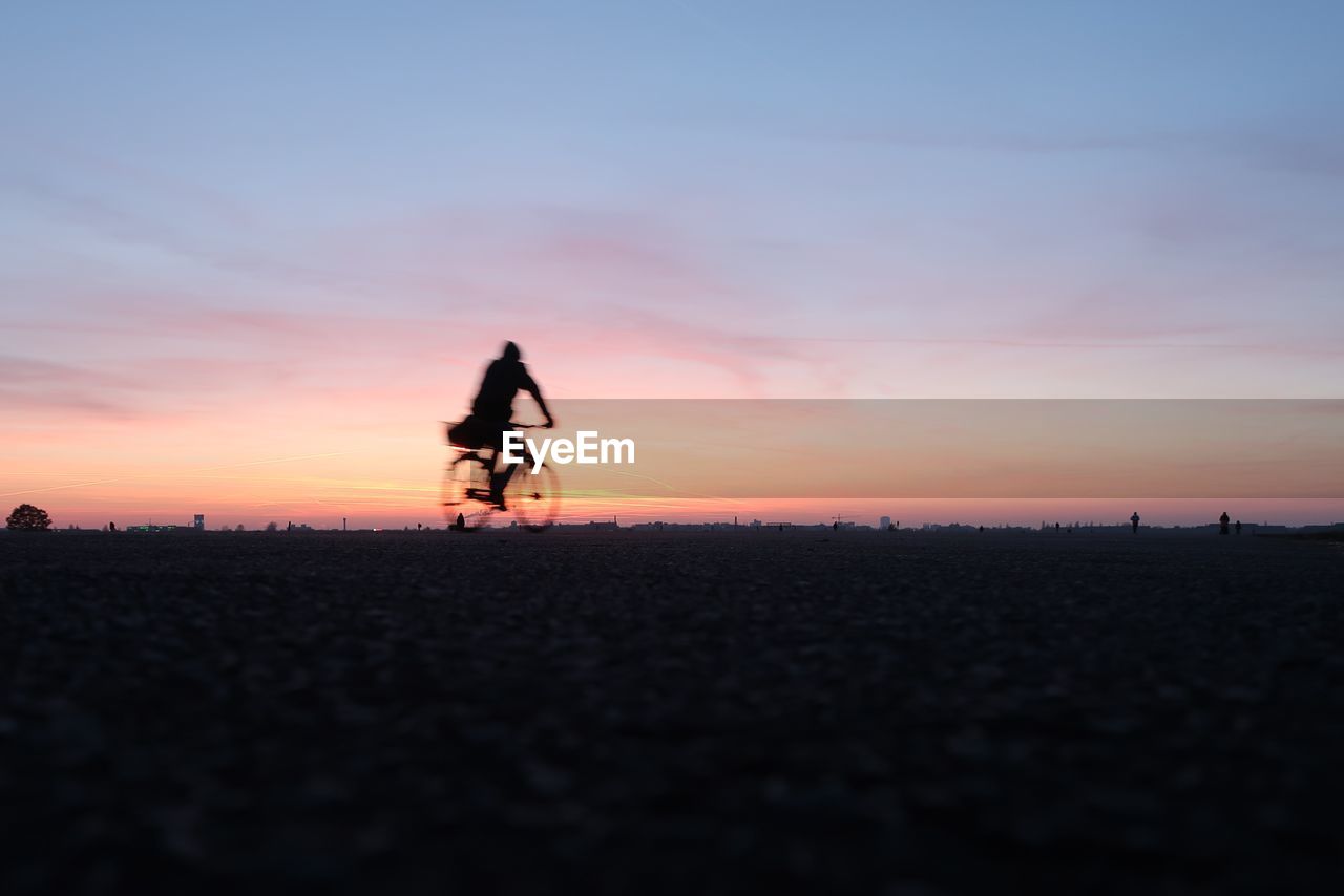 SILHOUETTE MAN RIDING BICYCLE ON ROAD AGAINST SKY