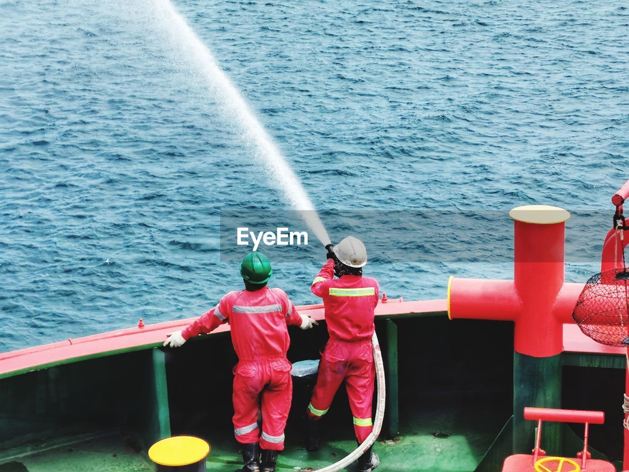 Rear view of firefighters spraying water while standing in nautical vessel