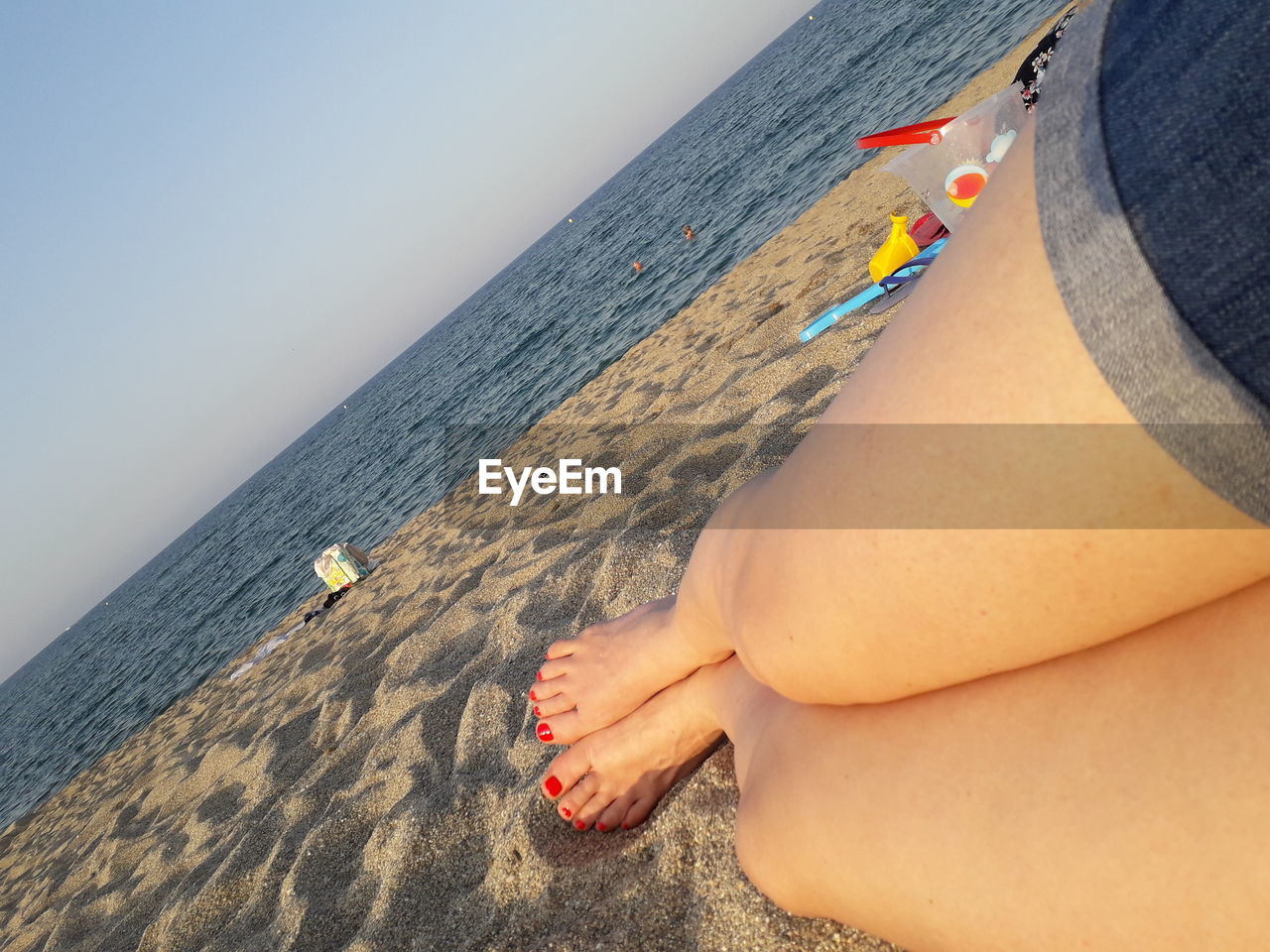 Low section of woman lying at beach against clear sky