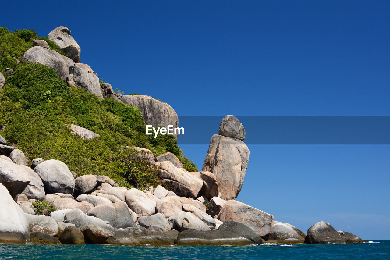 Rocks by sea against clear blue sky