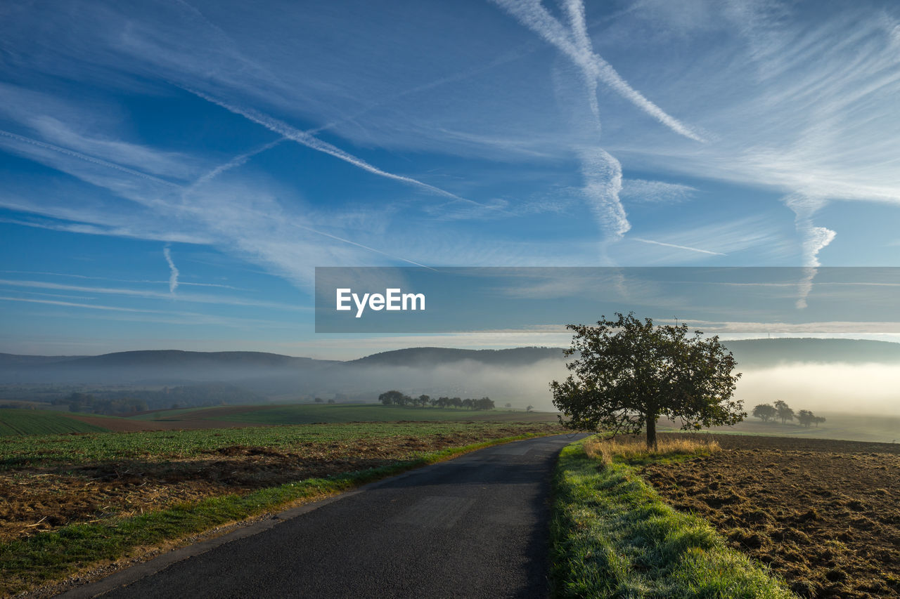 Road by trees on field against sky