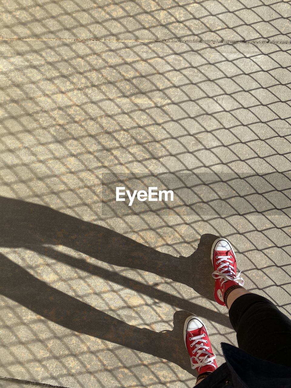 LOW SECTION OF PERSON ON FOOTPATH BY SHADOW ON STREET