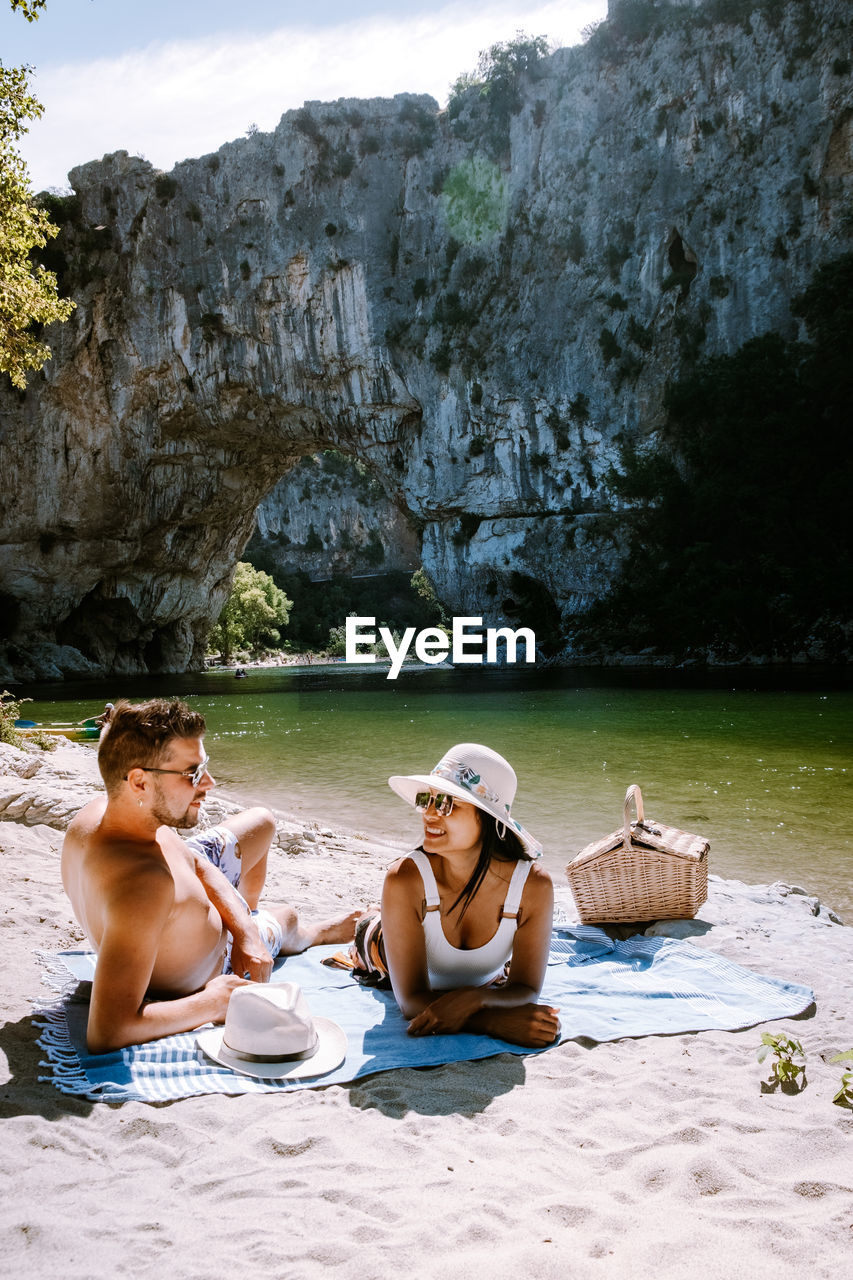 Full length of couple relaxing on beach against rock formation