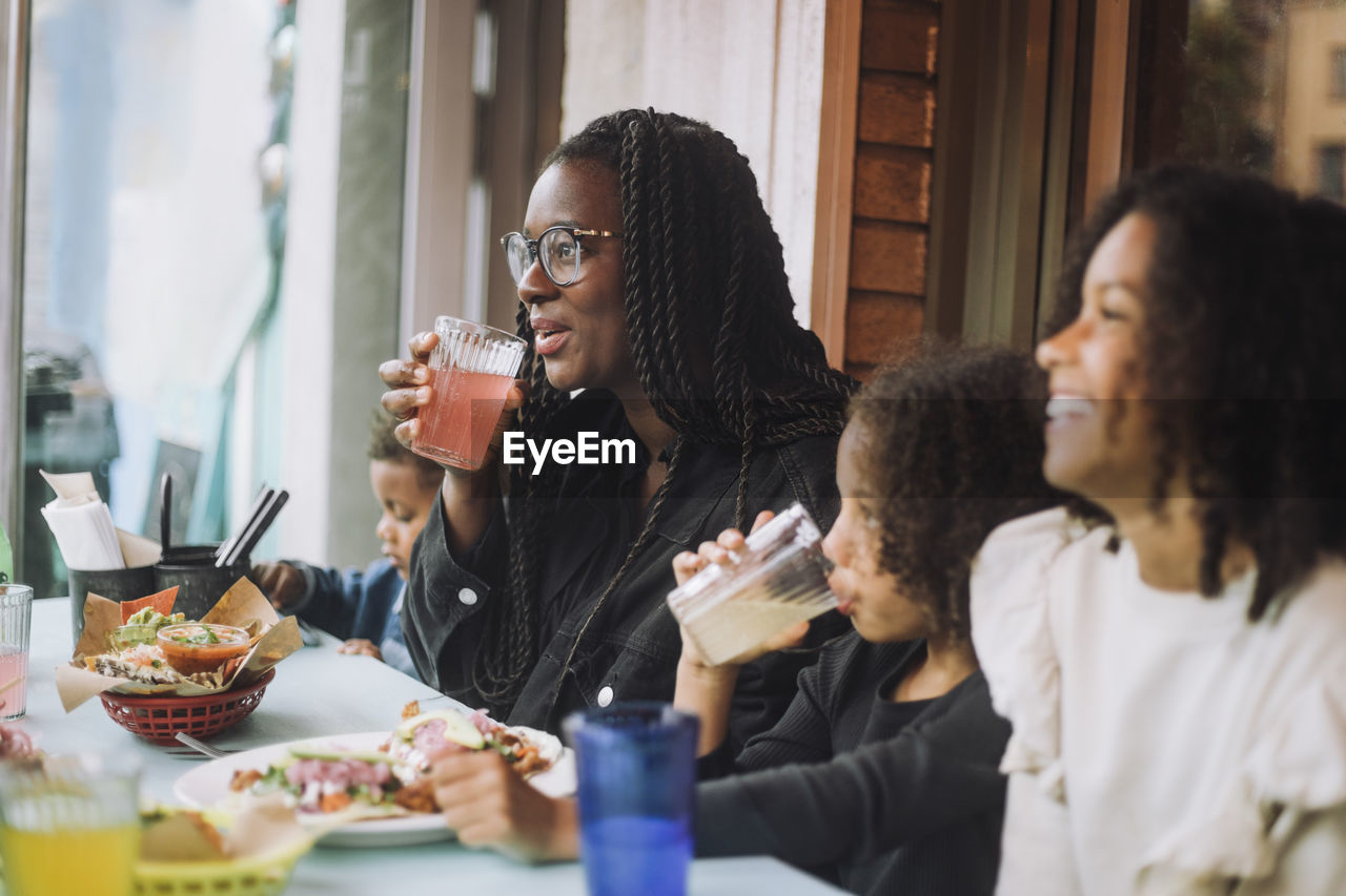 Smiling woman enjoying food and drinks with children while sitting at restaurant