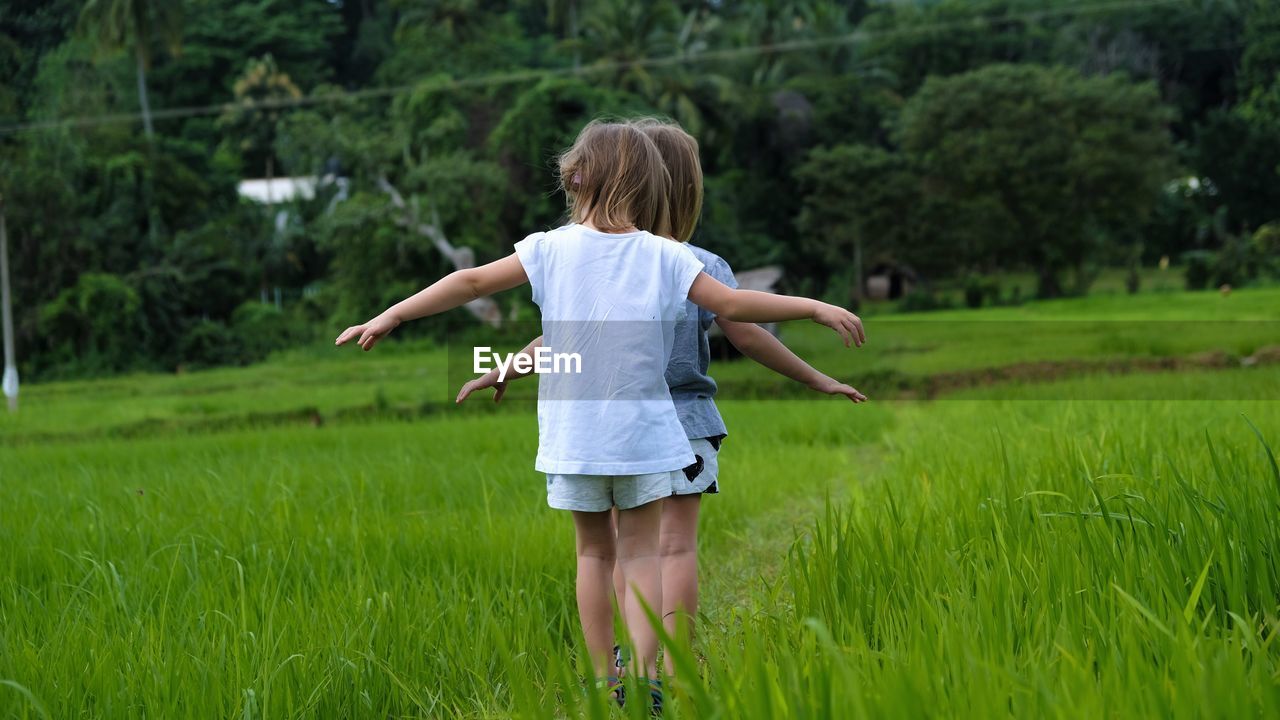 Rear view of girls standing by plants on field