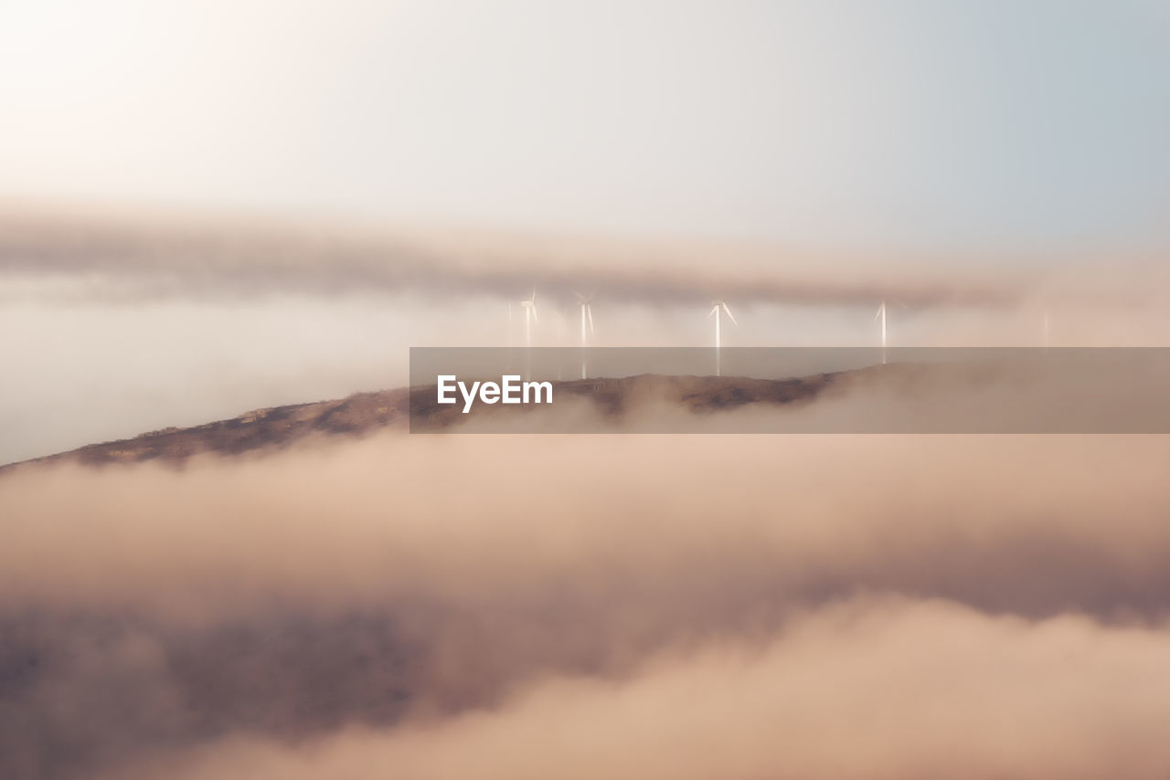 Windmills of modern wind power station located on hill in misty morning in countryside