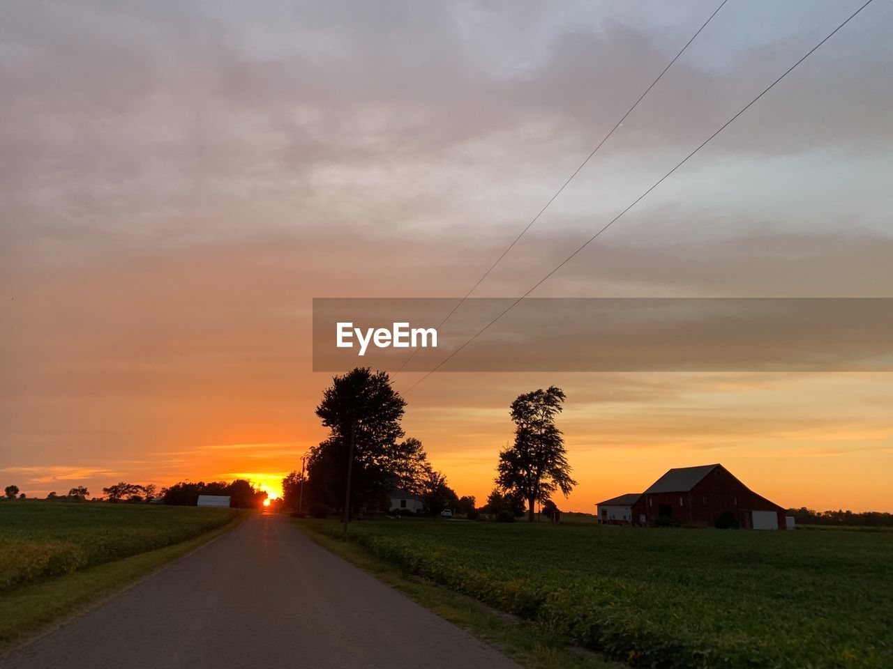 Country road amidst field against sky during sunset with barn