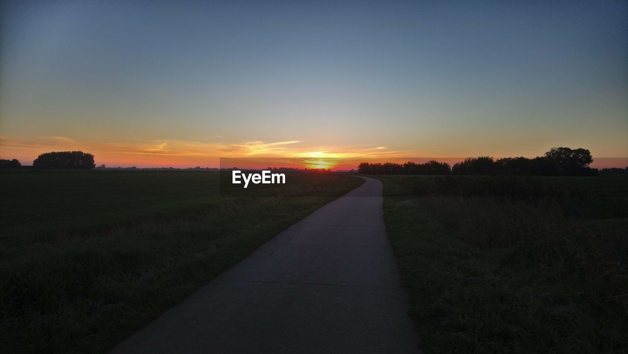 SCENIC VIEW OF ROAD AMIDST FIELD AGAINST SKY AT SUNSET
