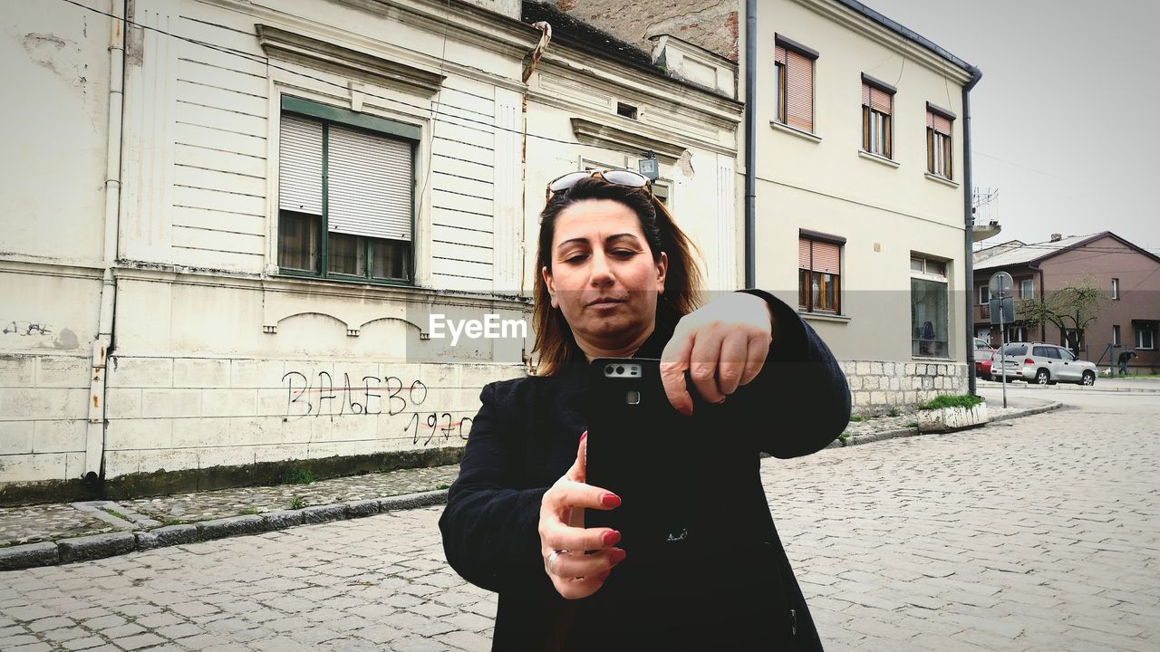 Mature woman taking selfie while standing on footpath against buildings