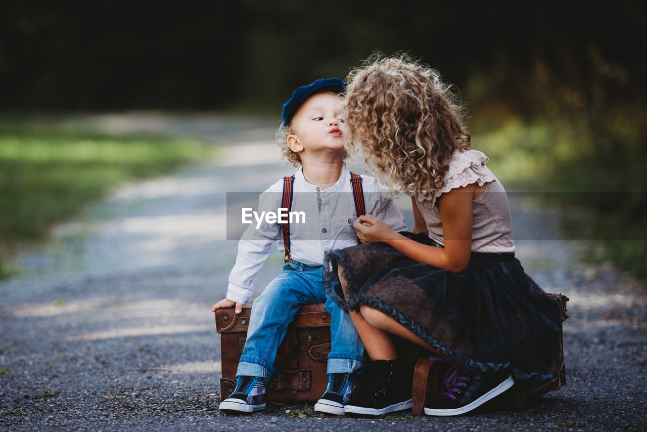 Adorable children siting on a vintage suitcase throwing a kiss