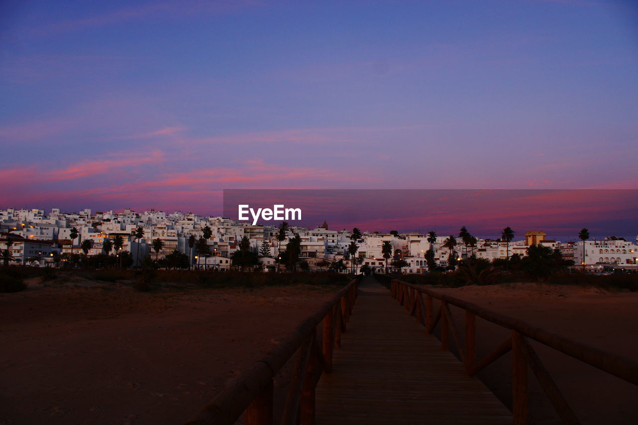 Footpath amidst buildings in city at sunset