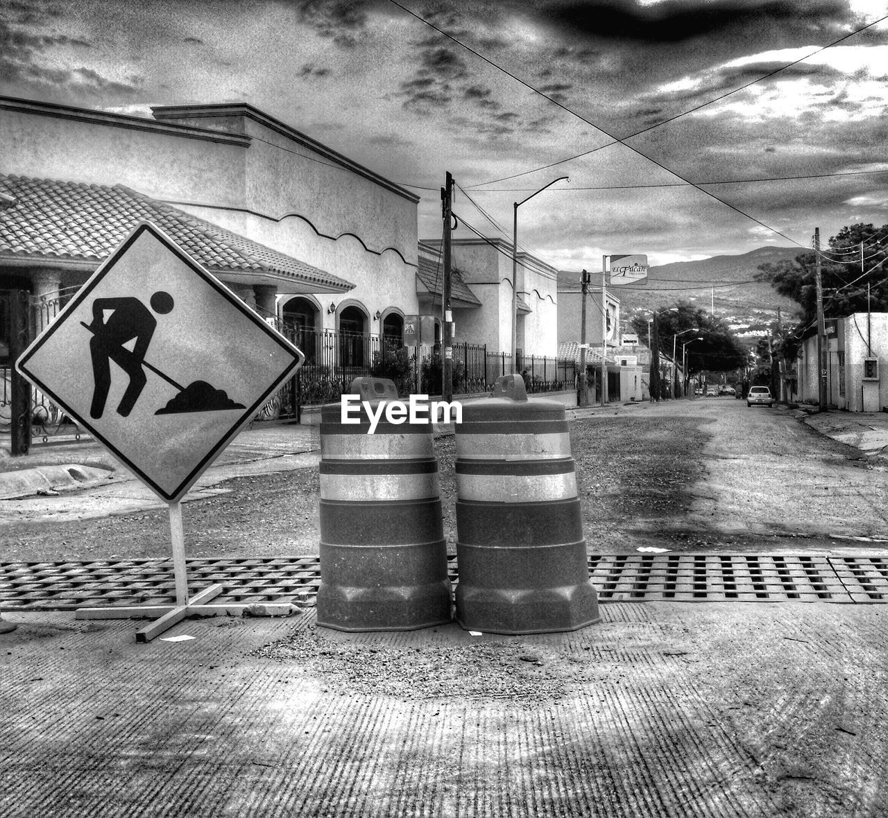 Sign board on street by buildings against cloudy sky