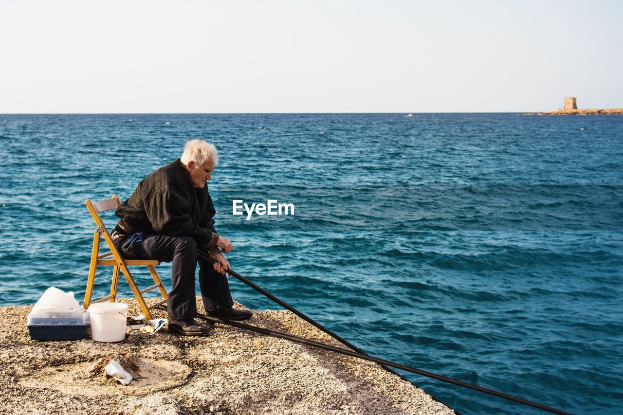 MAN STANDING ON SEA AGAINST CLEAR SKY