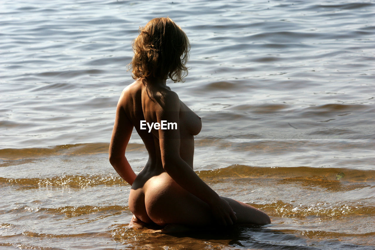 Sensuous naked young woman kneeling on shore at beach