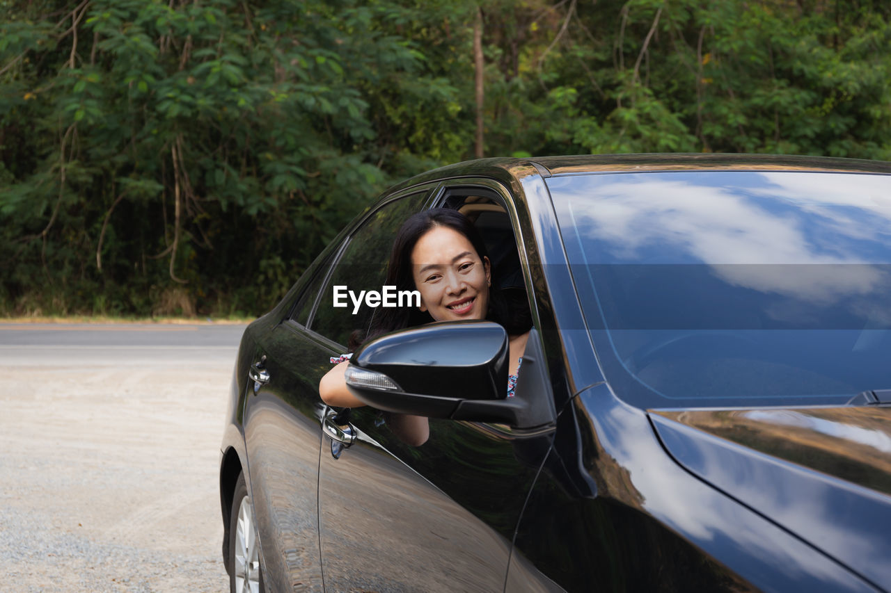 Cheerful woman looking out of car window smiles to camera.