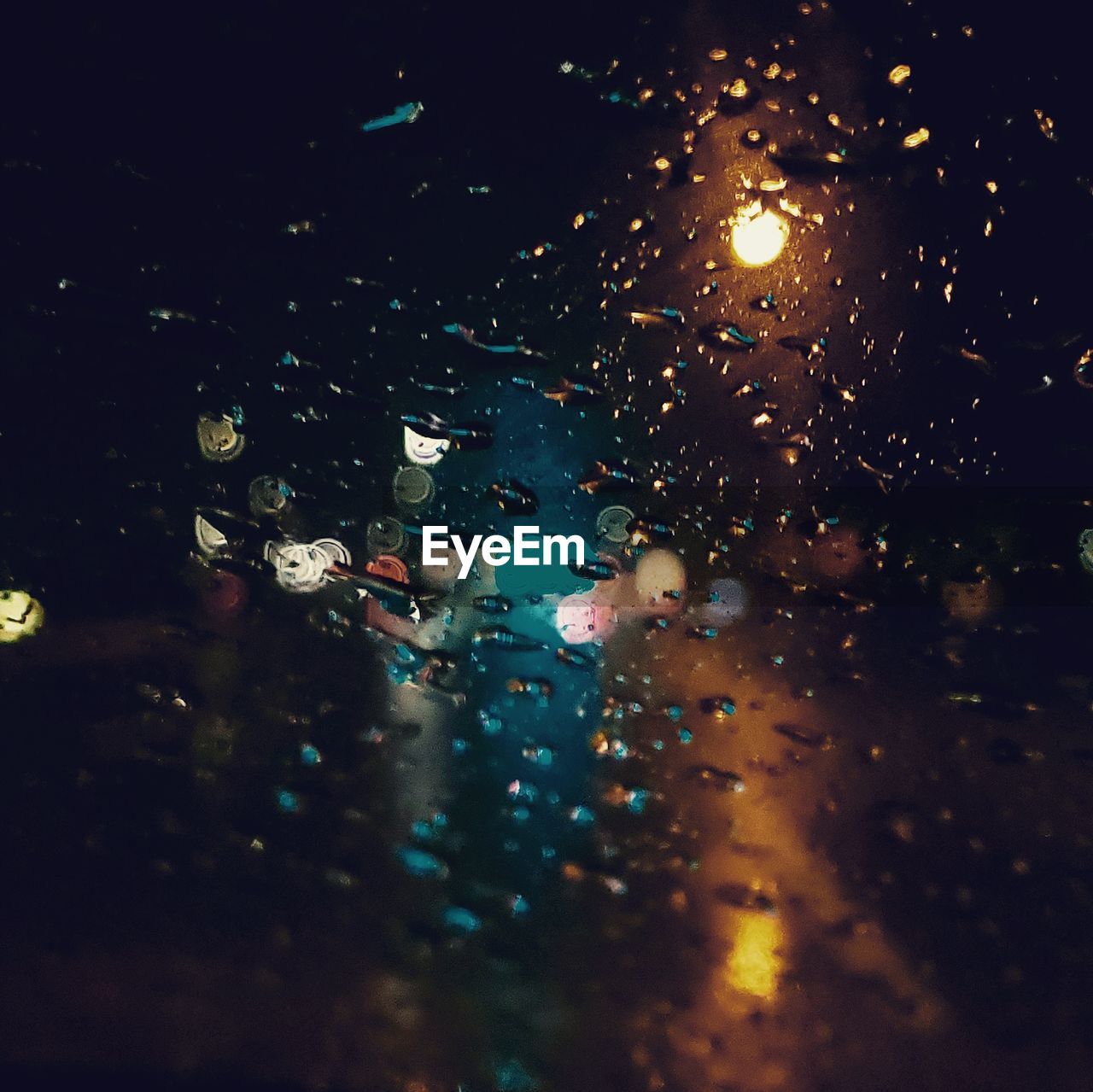 Illuminated lights seen through wet glass window of car
