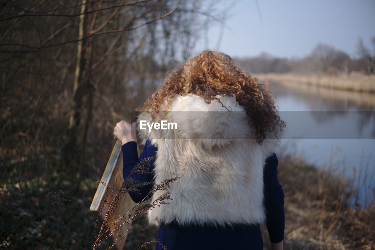 Rear view of woman in fur coat standing at lakeshore