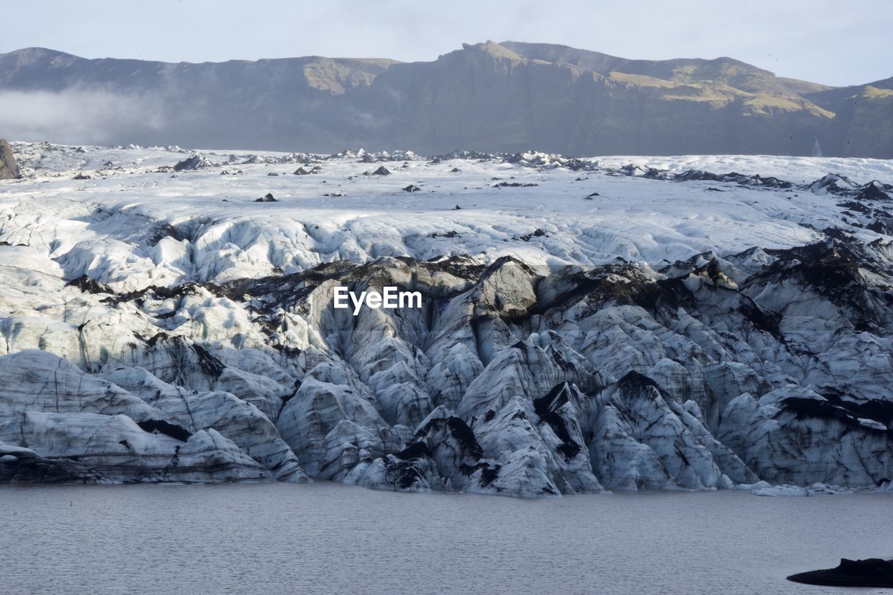 Scenic view of sea by mountains coverd in glacier ice against sky