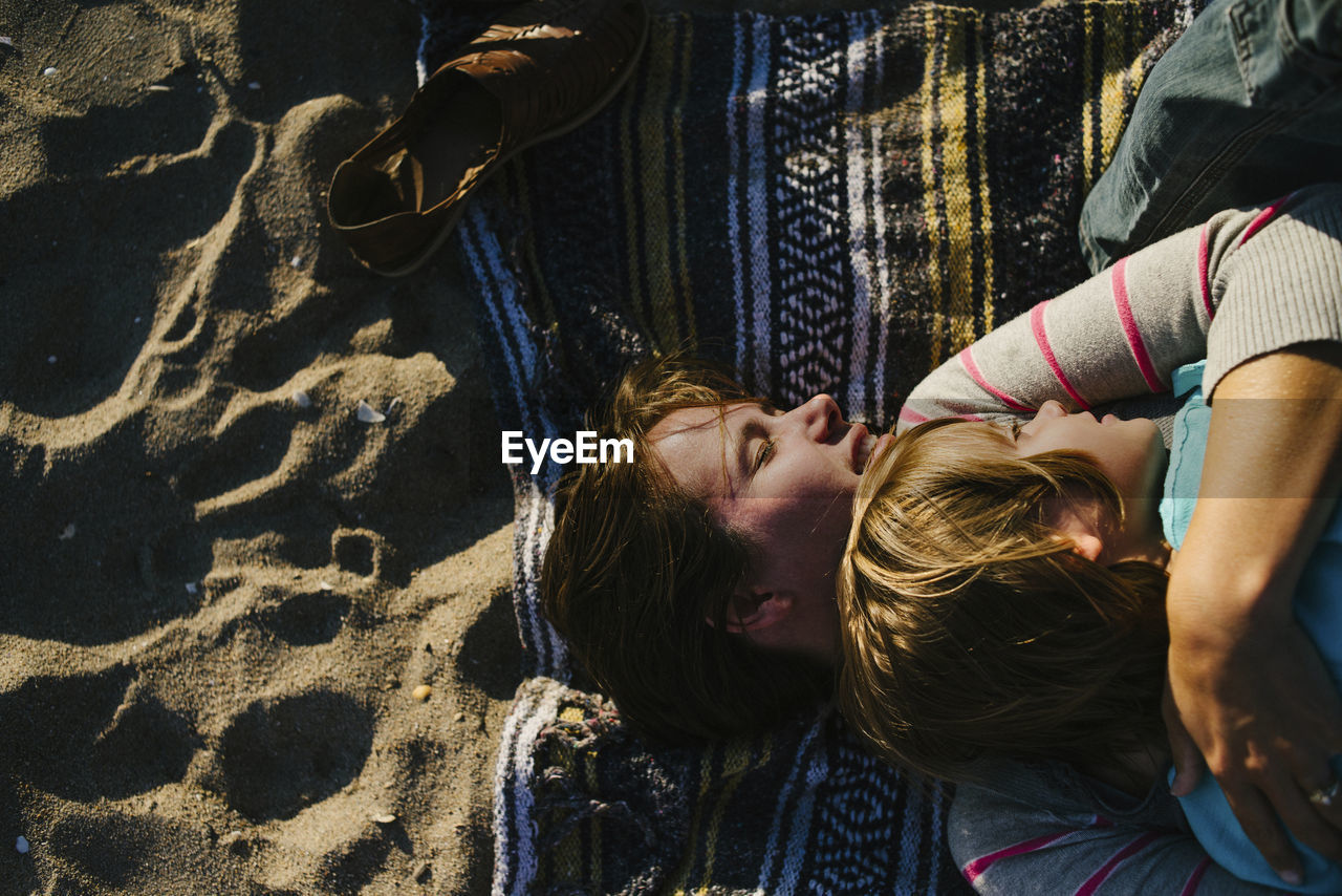 Overhead view of woman embracing daughter while lying on beach towel