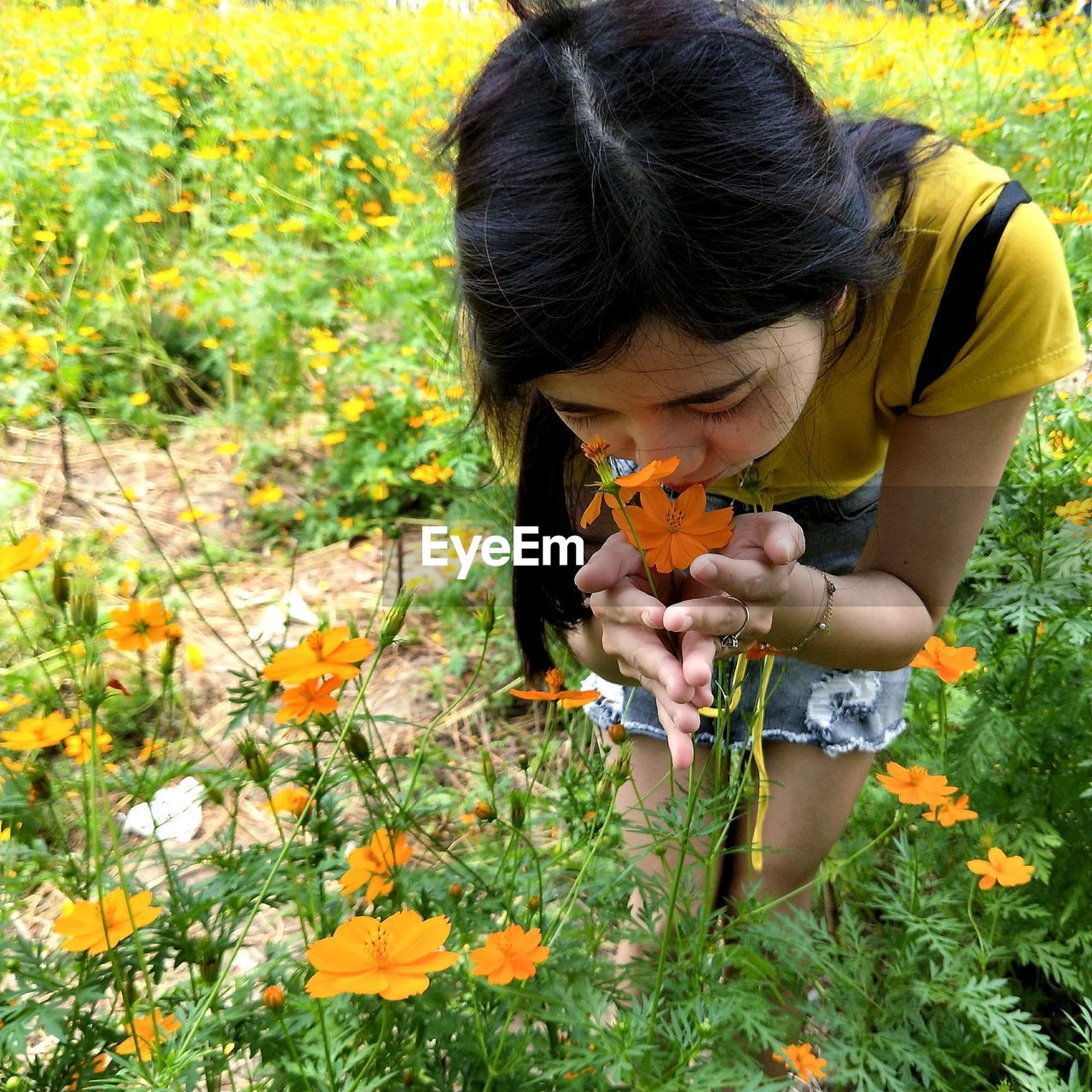 Close-up of woman smelling flowers on field