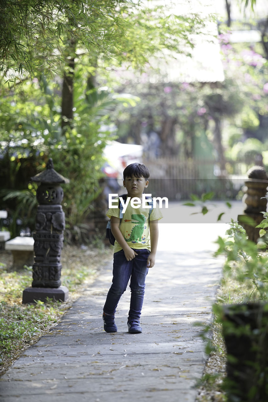 FULL LENGTH OF BOY STANDING ON FOOTPATH BY TREES