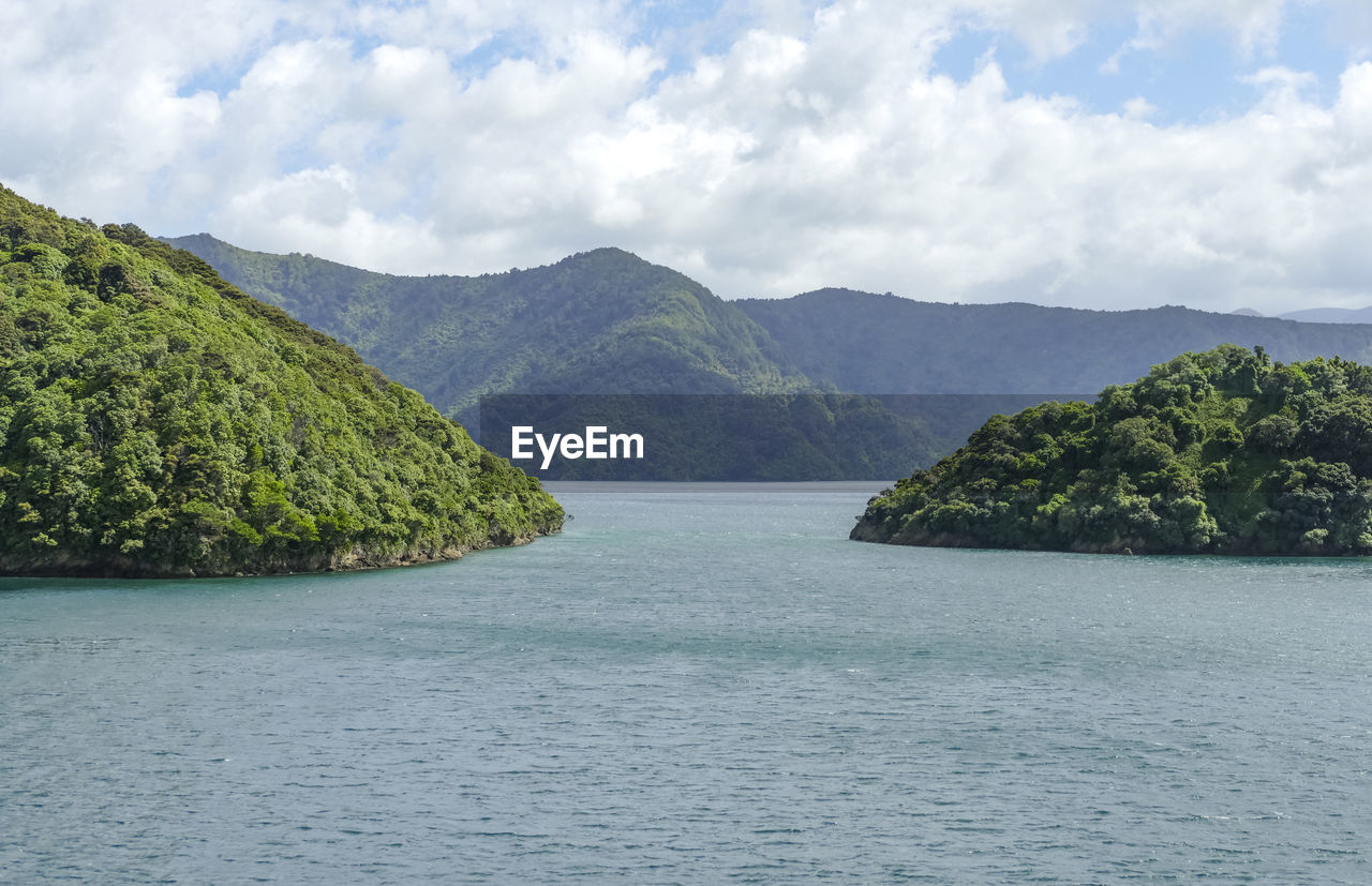 SCENIC VIEW OF SEA BY TREE MOUNTAINS AGAINST SKY