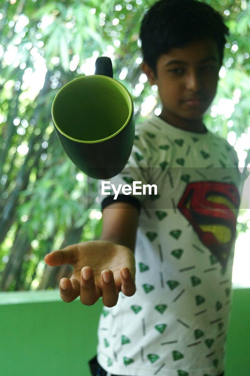 Boy catching cup while standing against trees