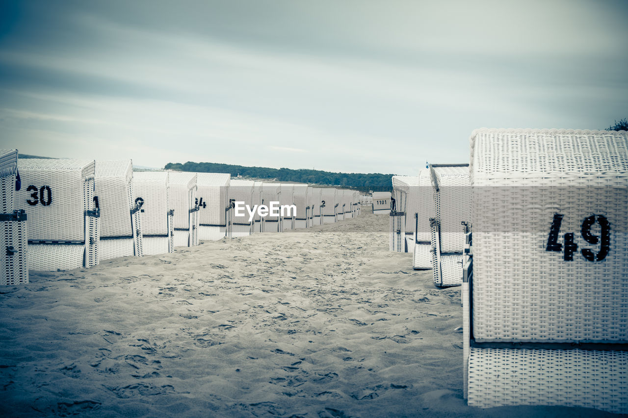 Hooded chairs on beach against sky