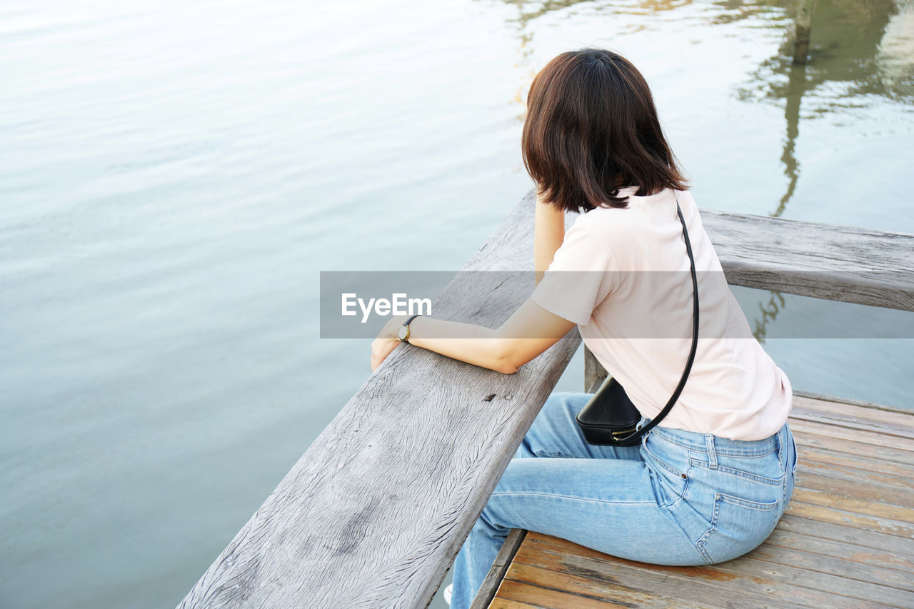 Side view of woman sitting on pier by lake