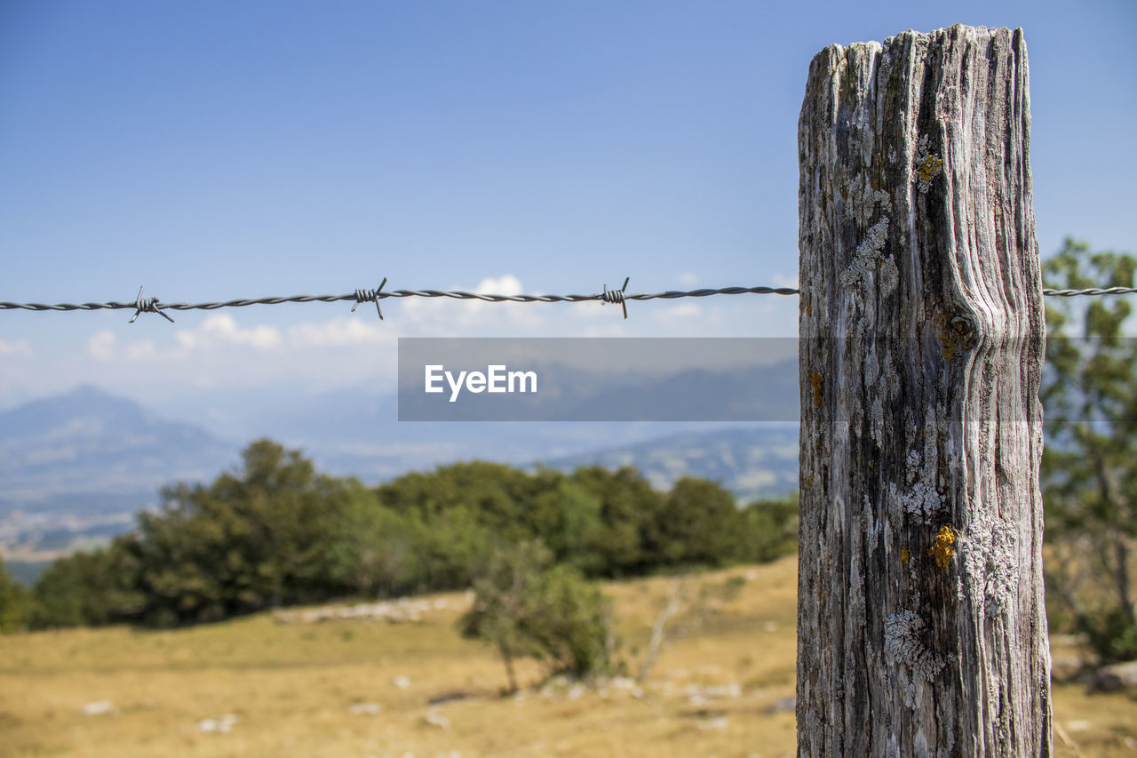 Barbed wire fence on field against scenic background