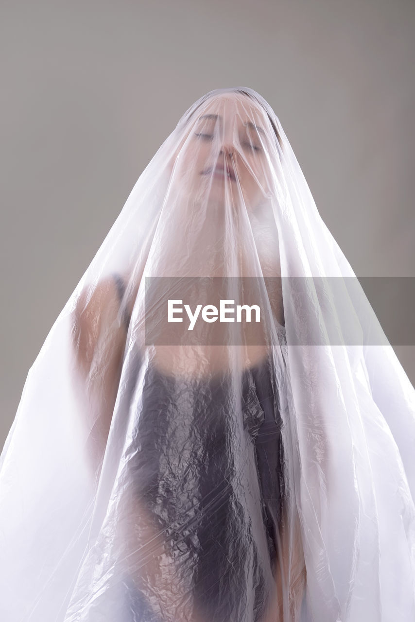 Close-up of woman covered in plastic over gray background