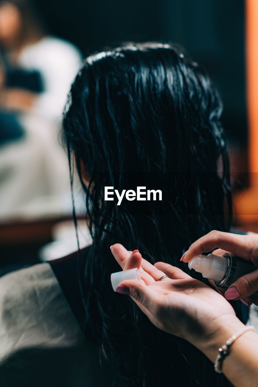 Cropped hands of hairdresser applying liquid to customer hair