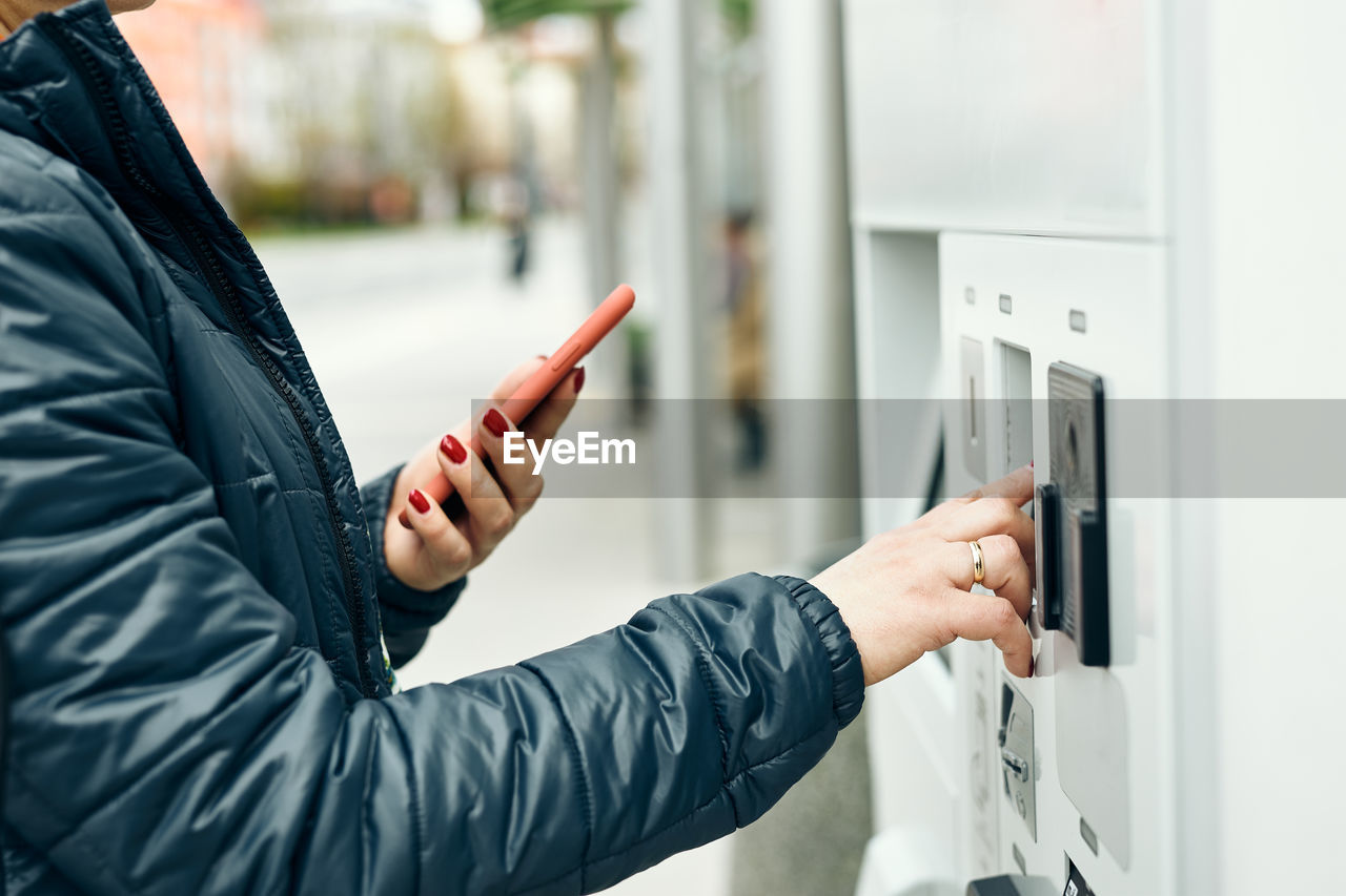 Woman buying ticket at ticket machine paying using mobile payment app on smartphone. buying tickets