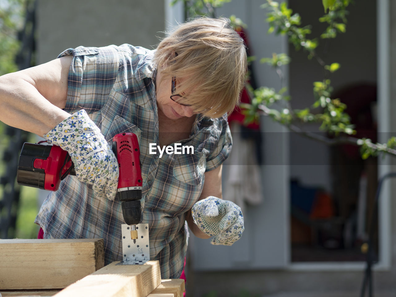 Senior caucasian woman assembles a wooden frame of building using metal fasteners using screwdriver