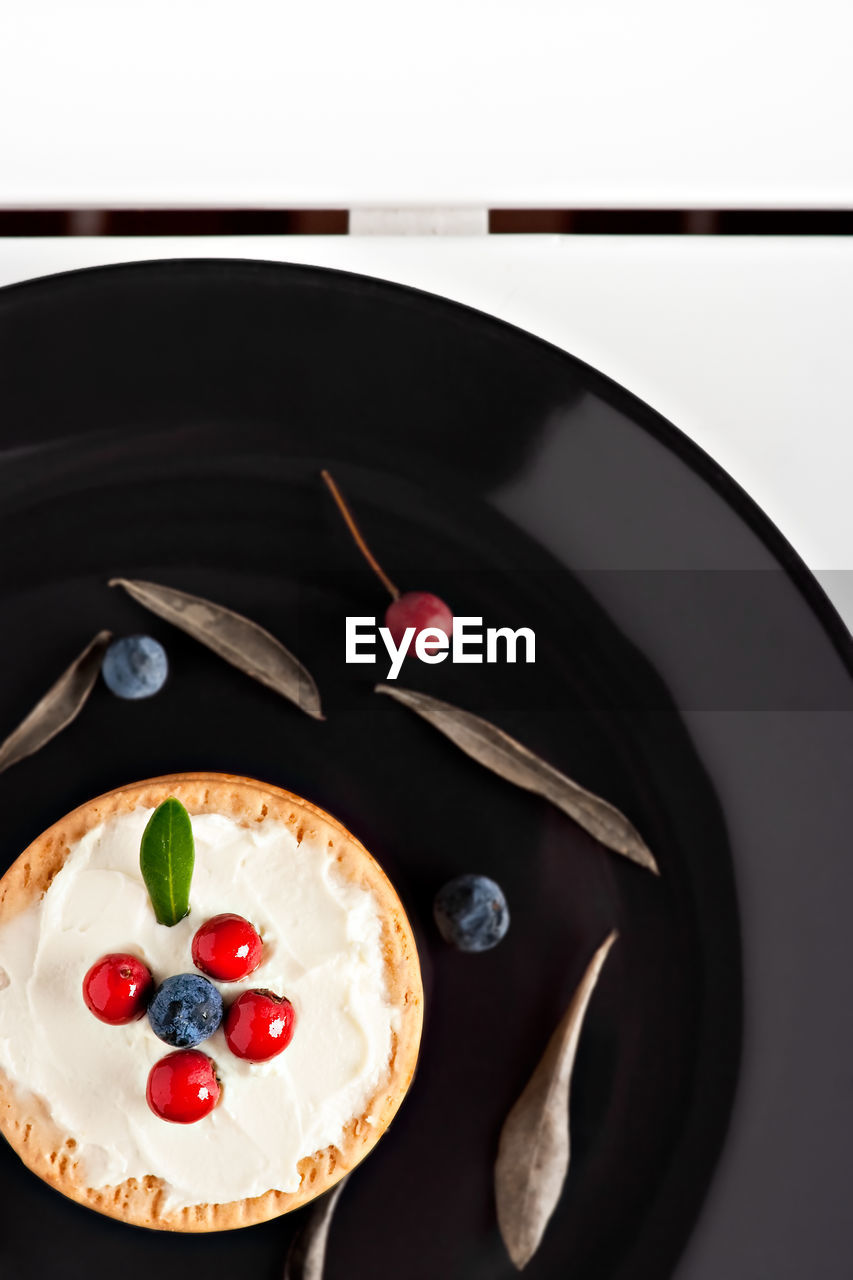 Cookies with cream cheese and blueberries in a dark plate surrounded with berries and dry leaves