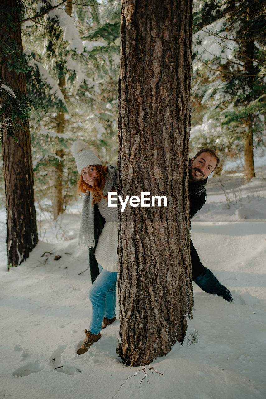 Portrait of couple standing by tree trunk during winter