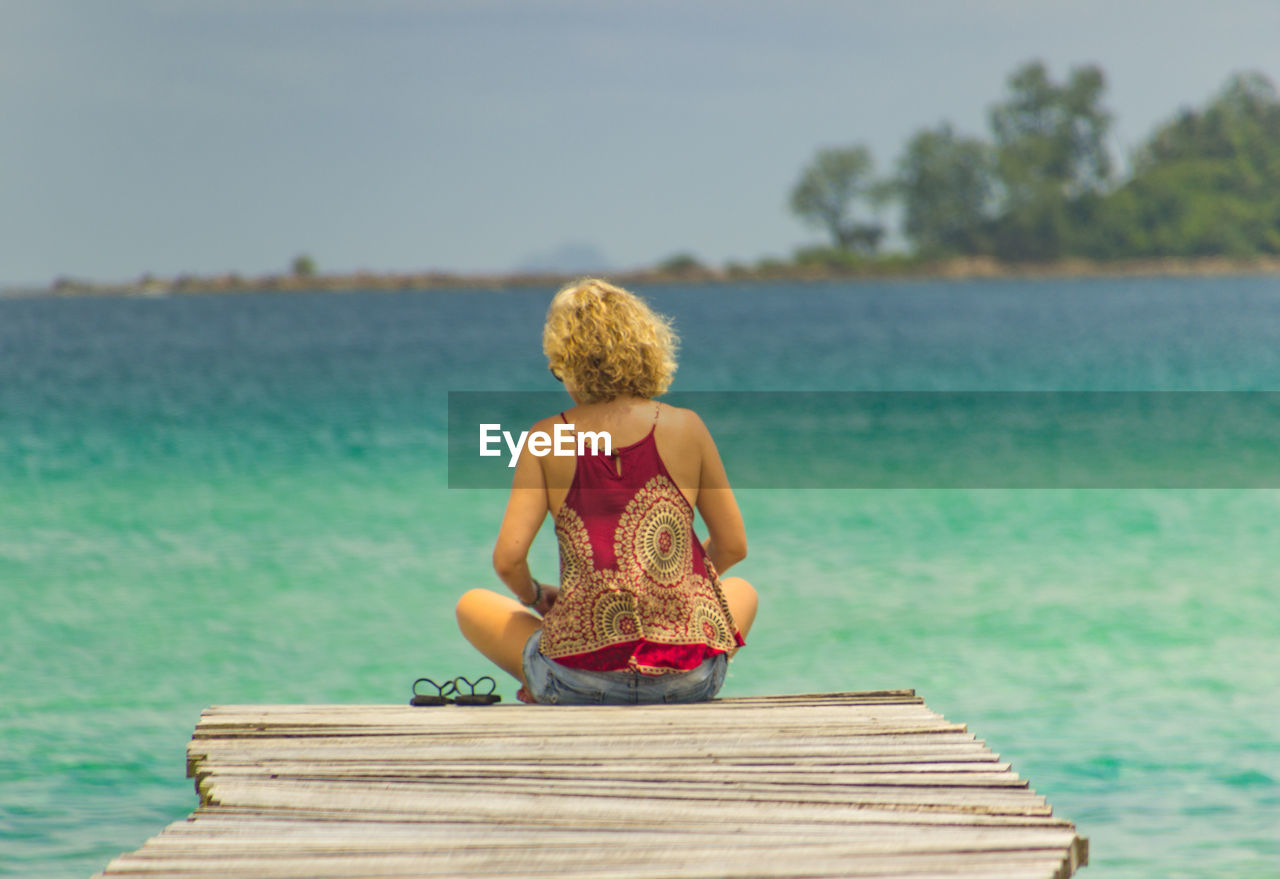 Rear view of woman sitting on pier against sea