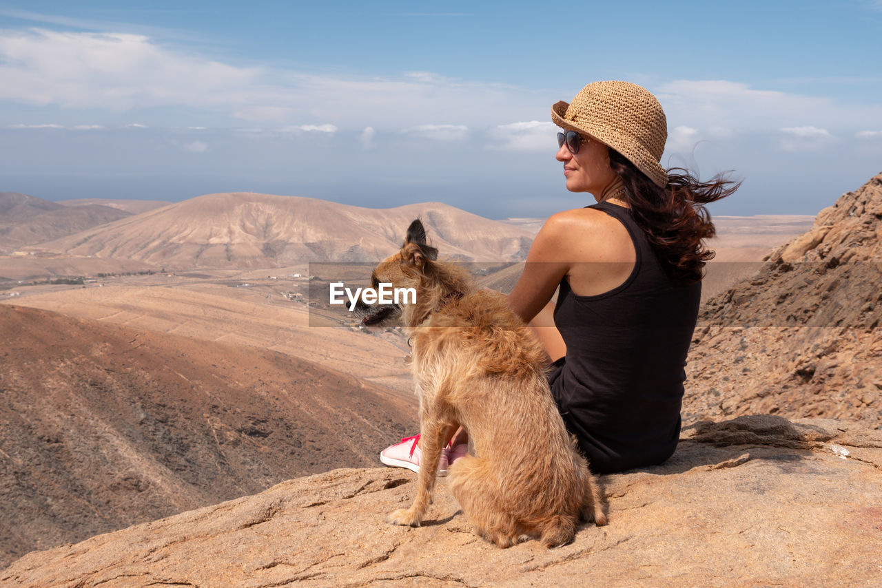 Woman with dog on rock against sky