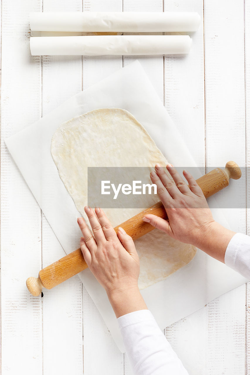 Woman hands spreading a very thin strudel dough with a rolling pin on a sheet of kitchen paper.